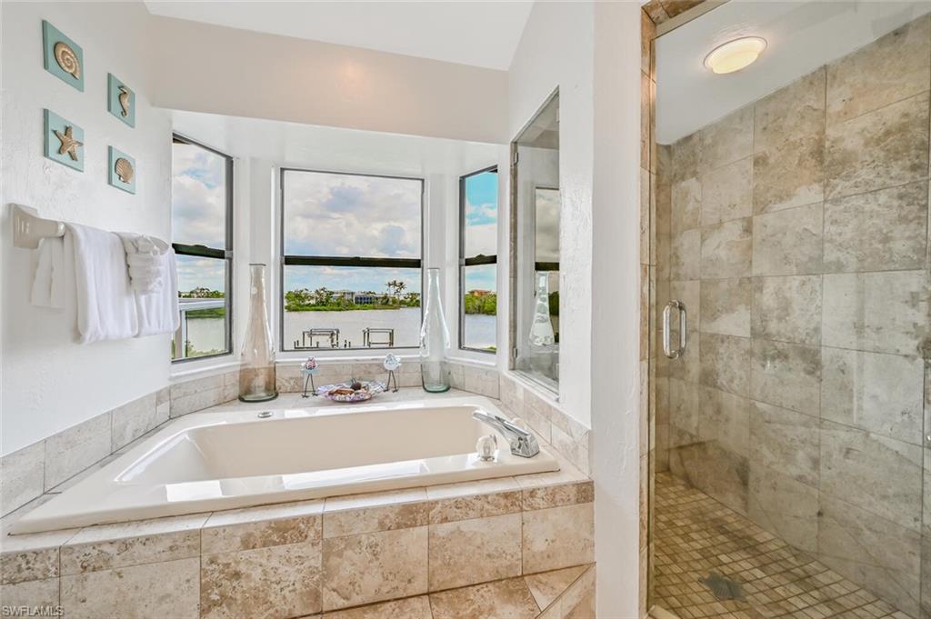 Corner soaking tub with a tiled surround, multiple windows, and a glass-enclosed shower featuring tiled walls and a mosaic tile floor