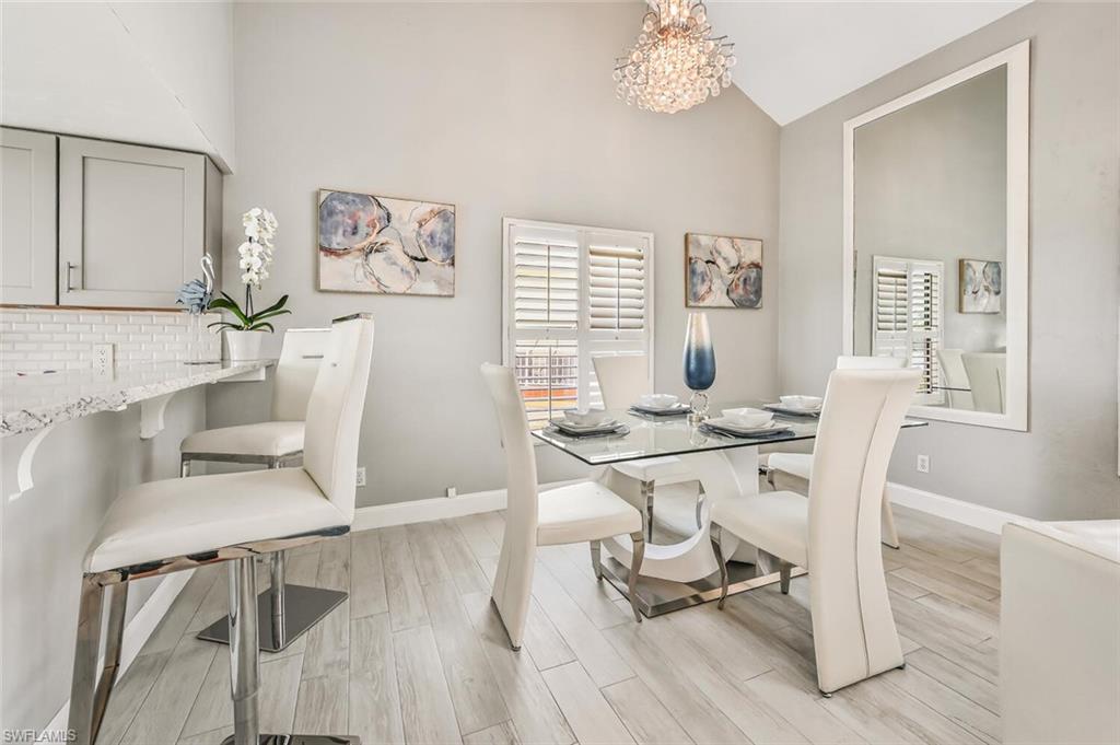 Dining area featuring a vaulted ceiling with a crystal chandelier, wood-finish flooring, plantation shutters, and a breakfast bar with a white tile backsplash