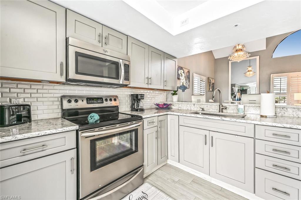 Kitchen featuring light gray shaker cabinetry with stainless steel hardware, white subway tile backsplash, and light-toned granite countertops