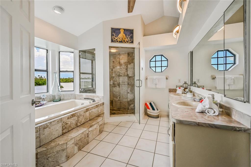 Spacious bathroom featuring a built-in soaking tub with stone tile surround, a walk-in shower with glass enclosure, a double vanity with undermount sinks and large mirror, and multiple windows