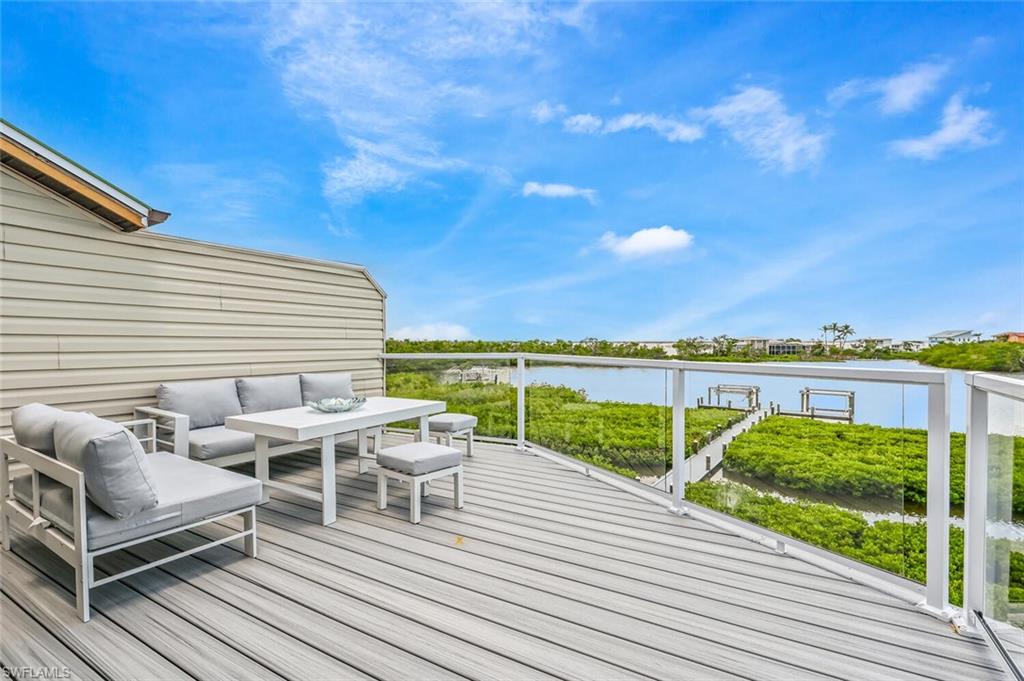 Expansive outdoor deck featuring composite decking, clear glass panel railings, and direct water frontage with a private dock structure