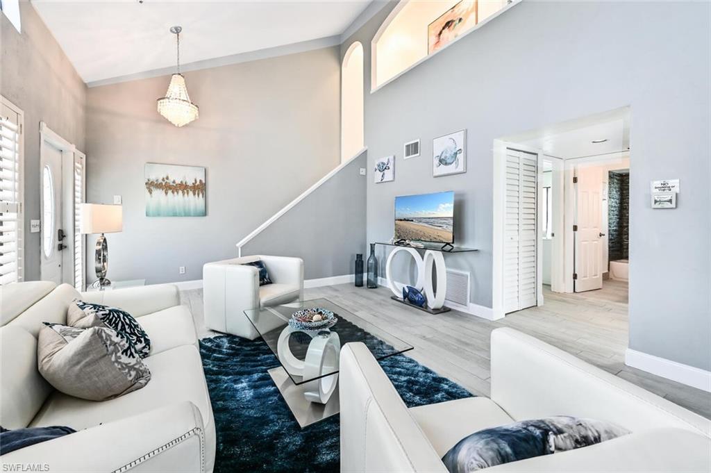 Vaulted ceiling living area featuring a chandelier, wood-finish flooring, a built-in staircase, and an arched transom window