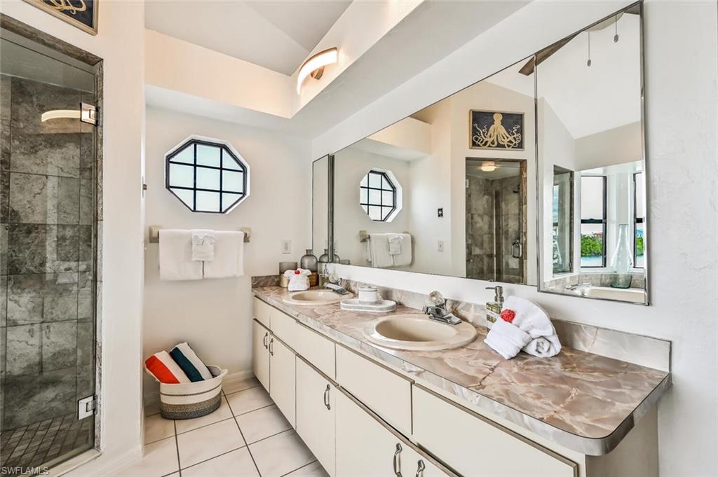 Bathroom featuring a dual vanity with a patterned countertop, a large wall-mounted mirror, and an octagon-shaped window
