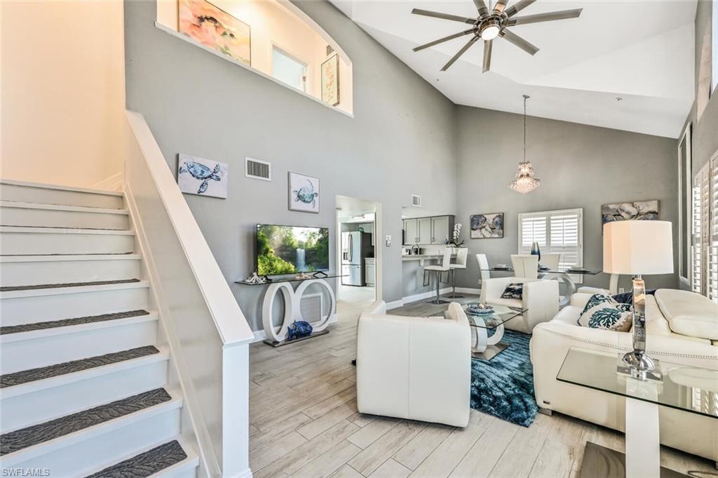 Vaulted ceiling living area featuring tile flooring, a contemporary ceiling fan, and plantation shutters