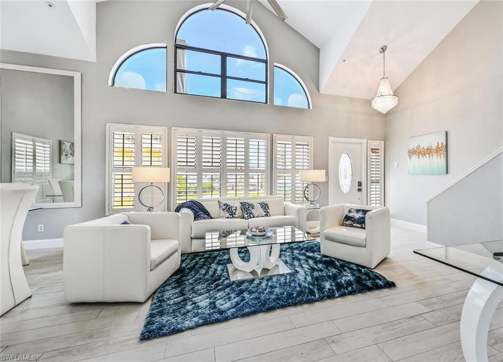 Two-story living area featuring vaulted ceilings, an arched window, plantation shutters, plank-style flooring, and a crystal chandelier