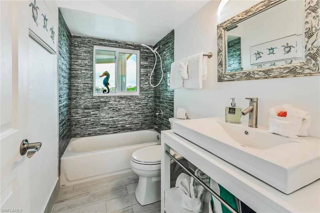 Bathroom featuring a white bathtub, a tiled shower surround, a window providing natural light, a white vanity with an integrated sink, and a framed mirror