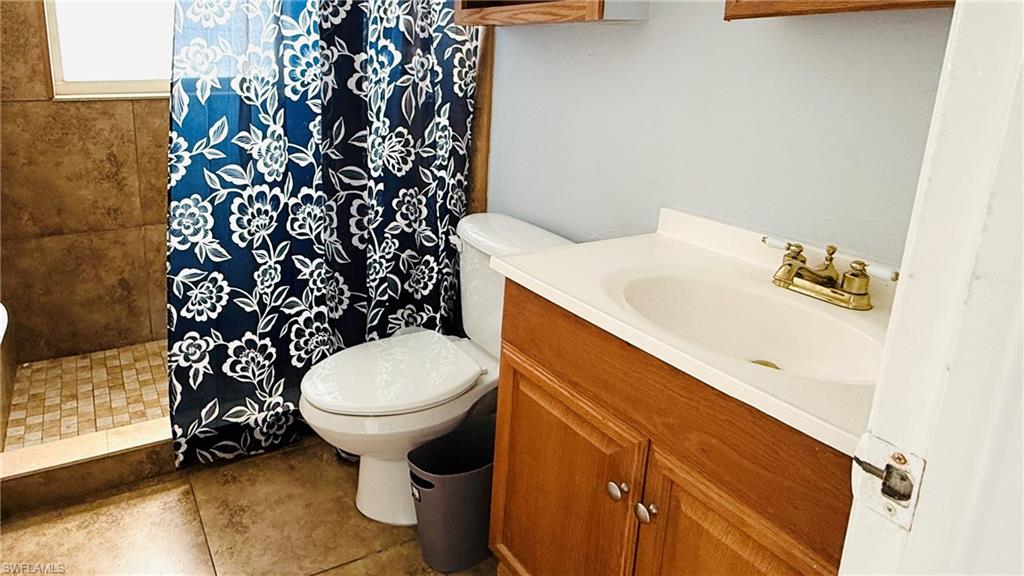 Walk-in shower with tiled walls and floor, wood-finish vanity with an integrated sink, and a brass-finish faucet