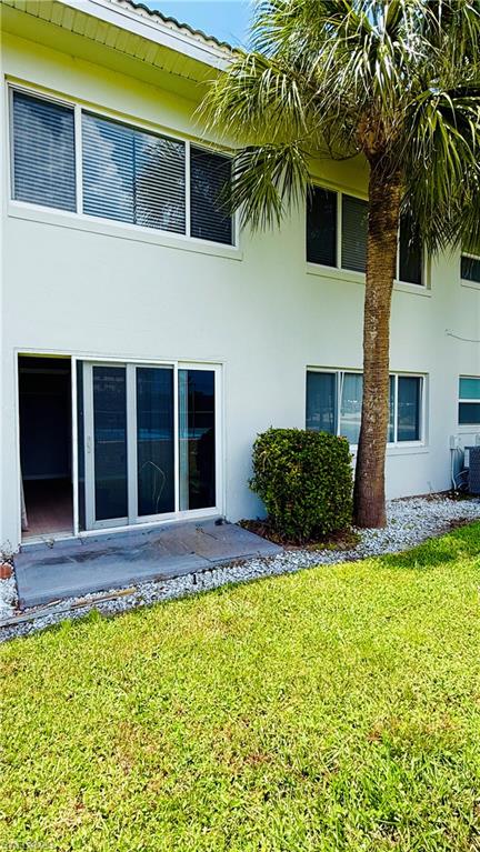 Modern residence featuring a spacious ground-level patio with sliding glass doors, lush manicured lawn, mature palm tree, and decorative stone landscaping