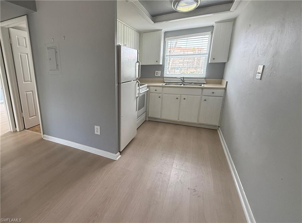 Wood-finish flooring throughout, white cabinetry with matching appliances, light-colored countertops, and a ceiling-mounted light fixture