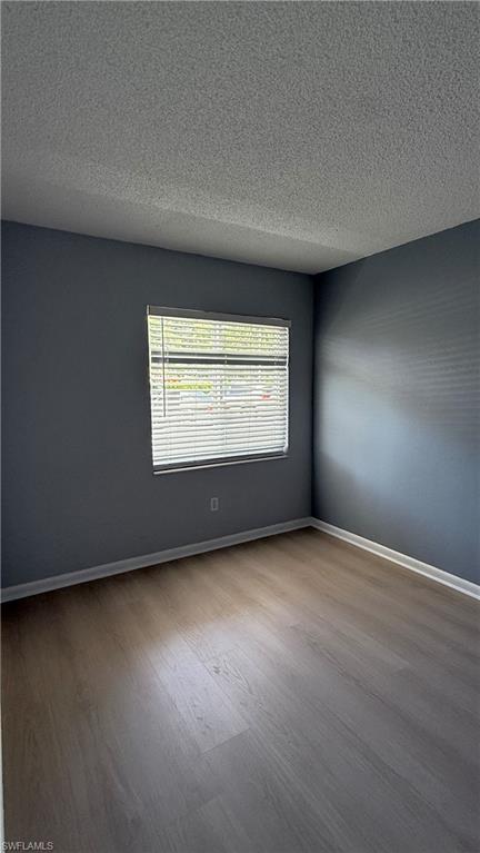 Wood-finish flooring, window with blinds, and white baseboards