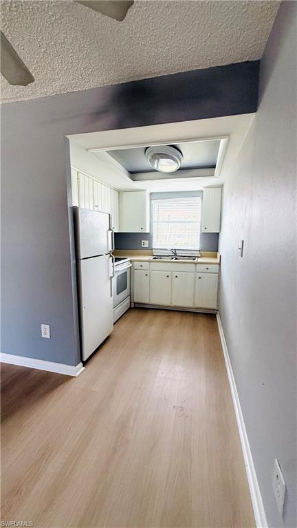 Compact kitchen featuring white cabinetry, a single basin sink, and a light-toned countertop