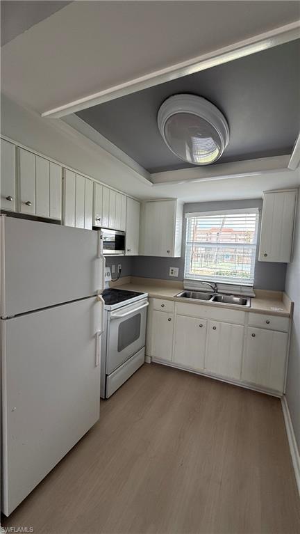 Compact kitchen featuring white cabinetry, stainless steel appliances including a smooth-top electric range, dual refrigerators, wood-finish flooring, and recessed ceiling lighting