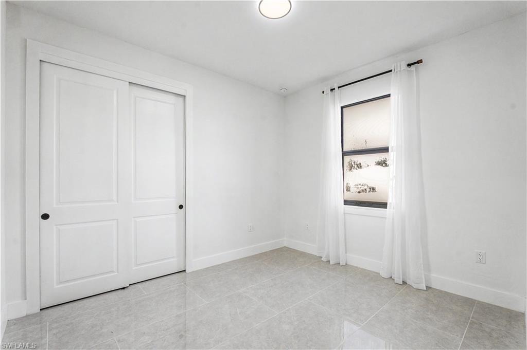 Bright interior space featuring light-toned tile flooring, clean white walls, and a window with white sheer curtains
