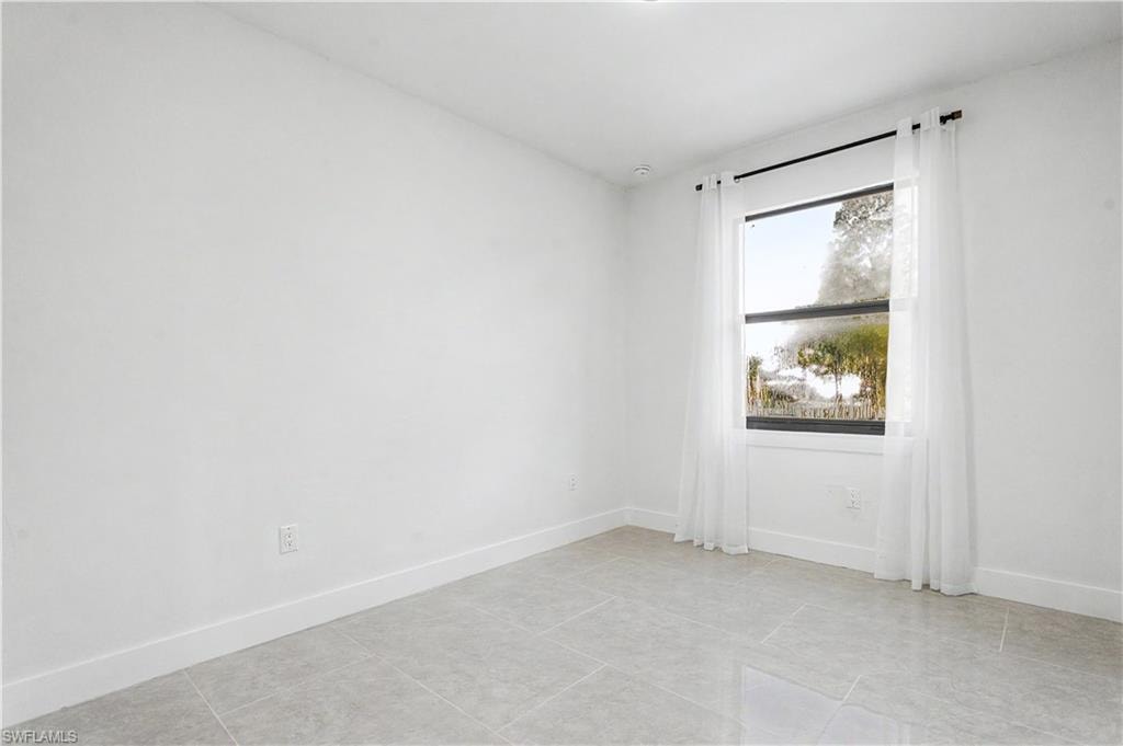 Bright room with light-toned tile flooring, white walls, and a large window with sheers