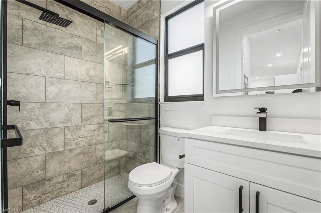 Modern bathroom featuring a frameless glass-enclosed shower with tile surround, a white vanity with integrated sink and matte black hardware, large illuminated mirror, and a low-profile toilet