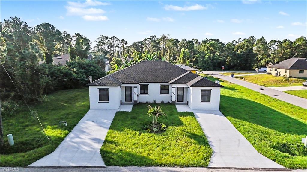 Duplex property featuring a white stucco exterior with black-framed windows, individual concrete driveways, and a central landscaped area with a small palm tree