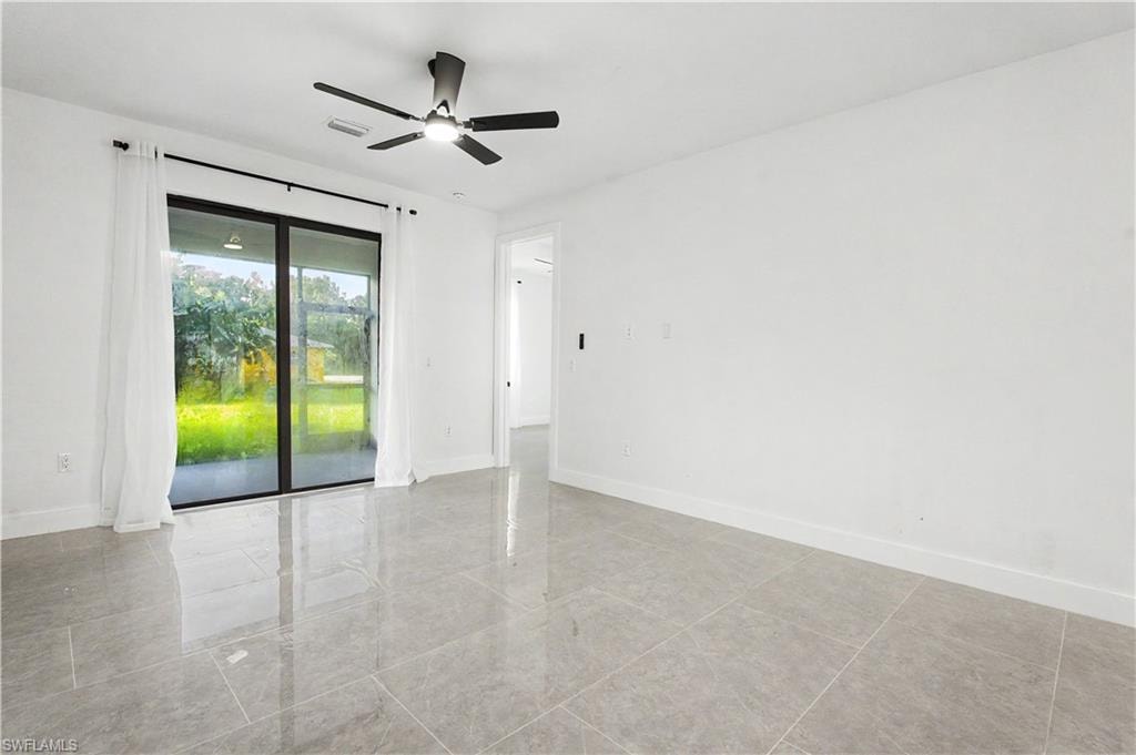 Spacious interior featuring large format gray tile flooring, a contemporary ceiling fan, and white baseboards