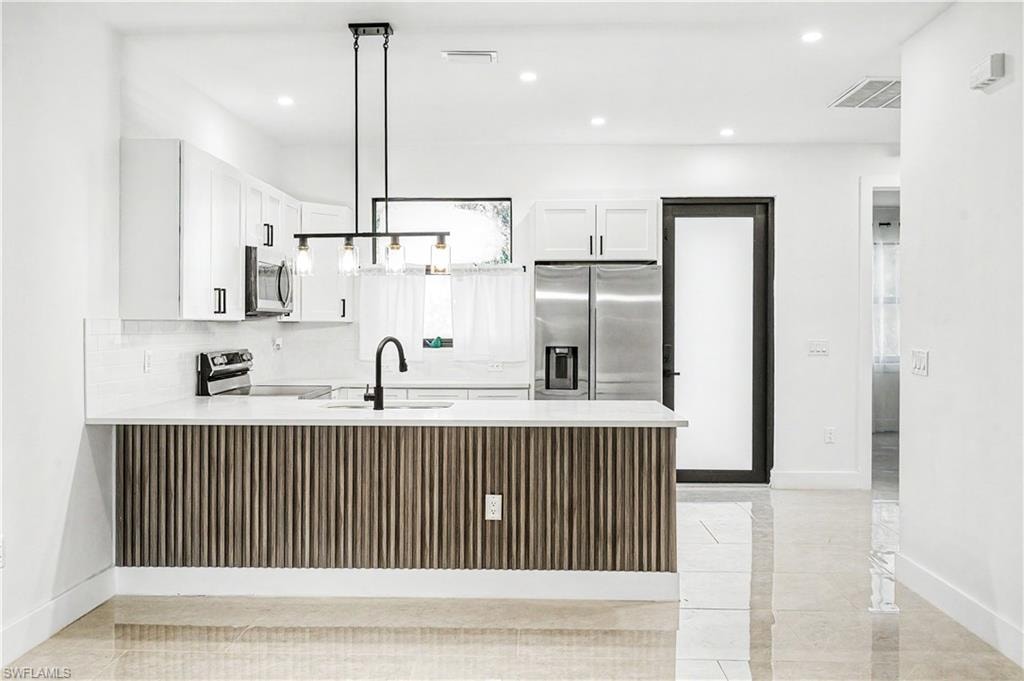 Kitchen featuring a slat wood-paneled island with a white countertop, white cabinetry with black hardware, stainless steel appliances, and a black gooseneck faucet