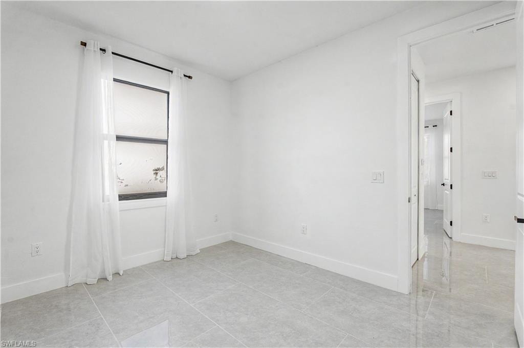 Room featuring light gray tile flooring, white baseboards, and a window with a black frame