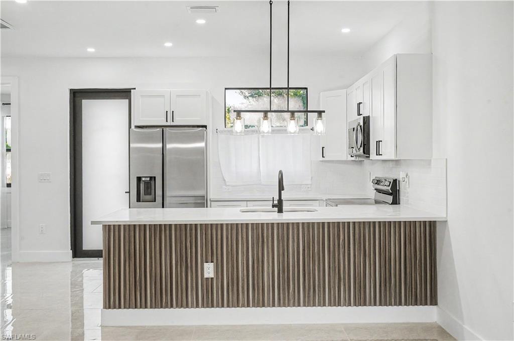 Modern kitchen featuring white cabinetry, stainless steel appliances, and a wood-slat island with a light-toned countertop