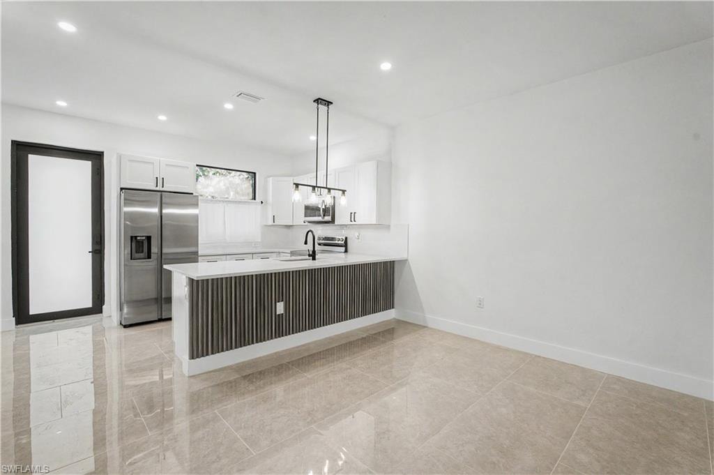 Contemporary kitchen featuring a large island with a textured panel base, stainless steel appliances, white cabinetry, and recessed lighting