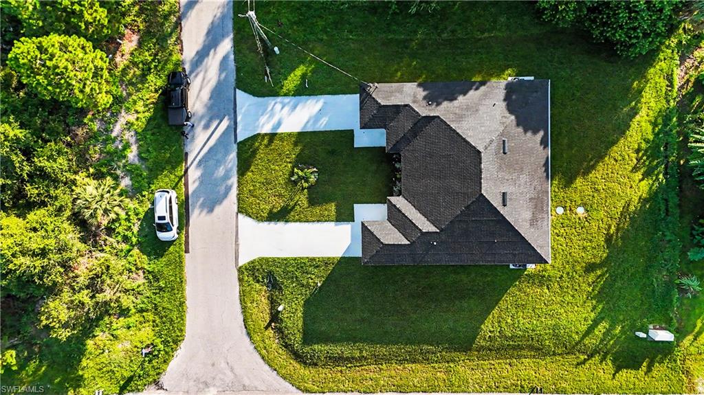 Contemporary residence featuring a dark shingle roof, lush green lawn, mature trees, and a paved driveway with multiple entrances