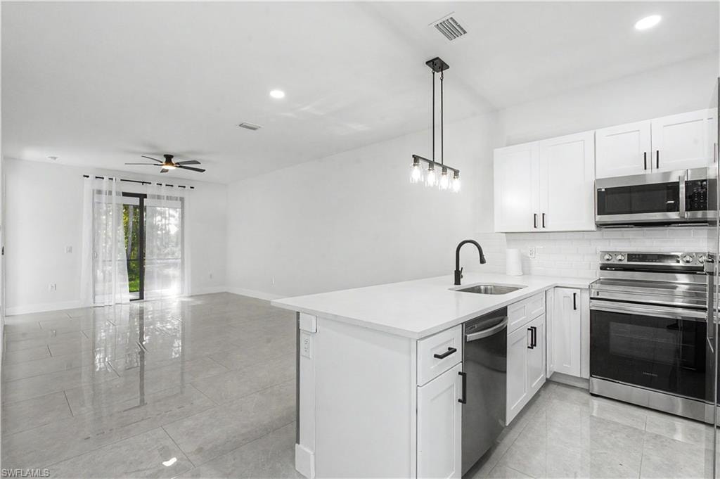 Open concept living space featuring a modern kitchen with white cabinetry, stainless steel appliances, and a central island with a sink
