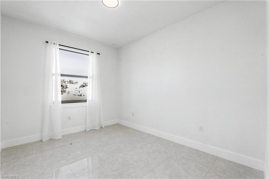 Bright room featuring light-colored tile flooring, white walls, and a window with a roller shade and sheer curtains