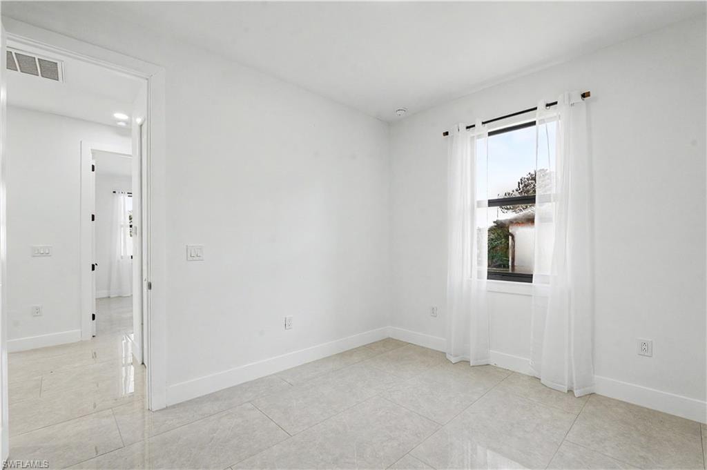 Bright interior room featuring a single window, light-toned tile flooring, white walls, white baseboards, and a doorway opening to an interior corridor