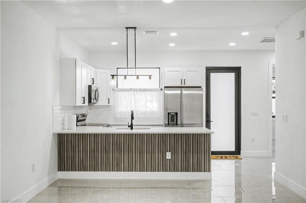 Modern kitchen featuring white cabinetry, subway tile backsplash, stainless steel appliances, and a central island with a fluted wood-finish accent panel