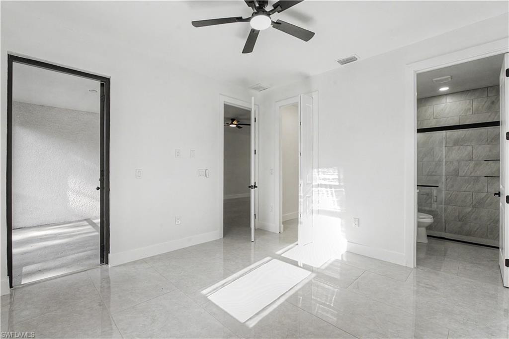 Spacious room with polished tile flooring, white walls, black ceiling fan, and access to a modern bathroom featuring tiled walls and a glass-enclosed shower