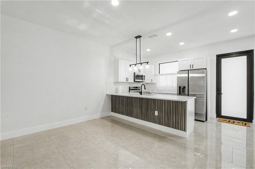 Open-concept kitchen and living area featuring a central island with a wood-slat base, white countertops, and a black pendant light fixture