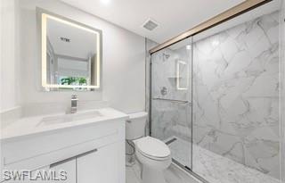 Bathroom featuring a white vanity with an integrated sink, illuminated mirror, and a glass-enclosed shower with large format marble-look tile