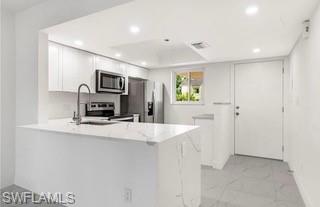 Modern kitchen featuring a waterfall peninsula with a sink, white cabinetry, stainless steel appliances, recessed lighting, and tiled flooring