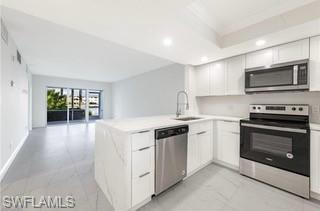 Modern kitchen featuring a waterfall-edge island with integrated sink, white cabinetry, stainless steel appliances, and tile flooring