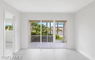 Spacious interior room with light-toned tile flooring and white walls, featuring a large sliding glass door opening to an outdoor patio with additional tile flooring