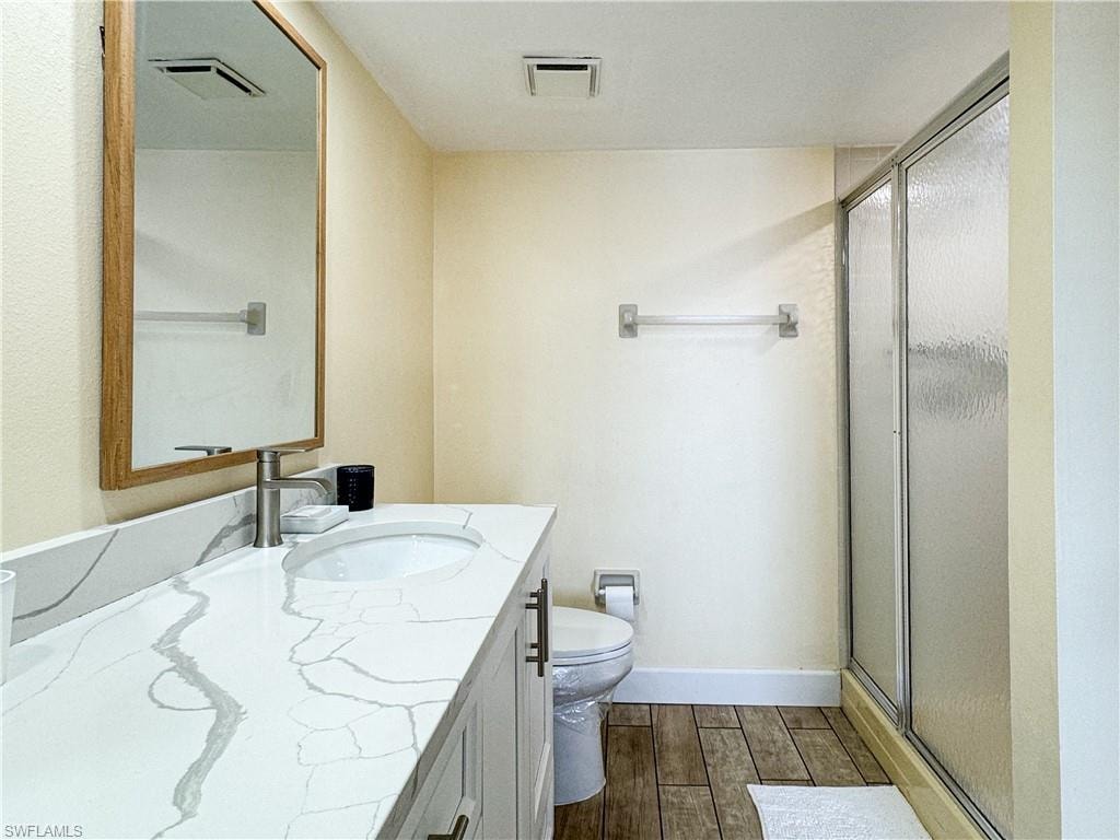 Bathroom with vanity, toilet, an enclosed shower, and hardwood / wood-style flooring