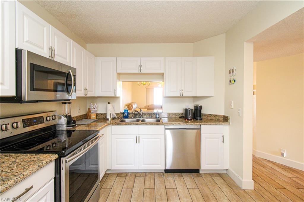 Kitchen with light wood-type flooring, white cabinets, appliances with stainless steel finishes, and sink