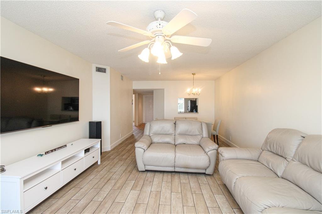 Living room featuring ceiling fan with notable chandelier, a textured ceiling, and light hardwood / wood-style flooring
