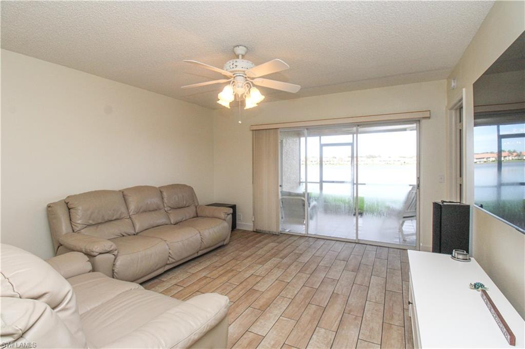 Living room with light hardwood / wood-style flooring, a water view, ceiling fan, and a textured ceiling