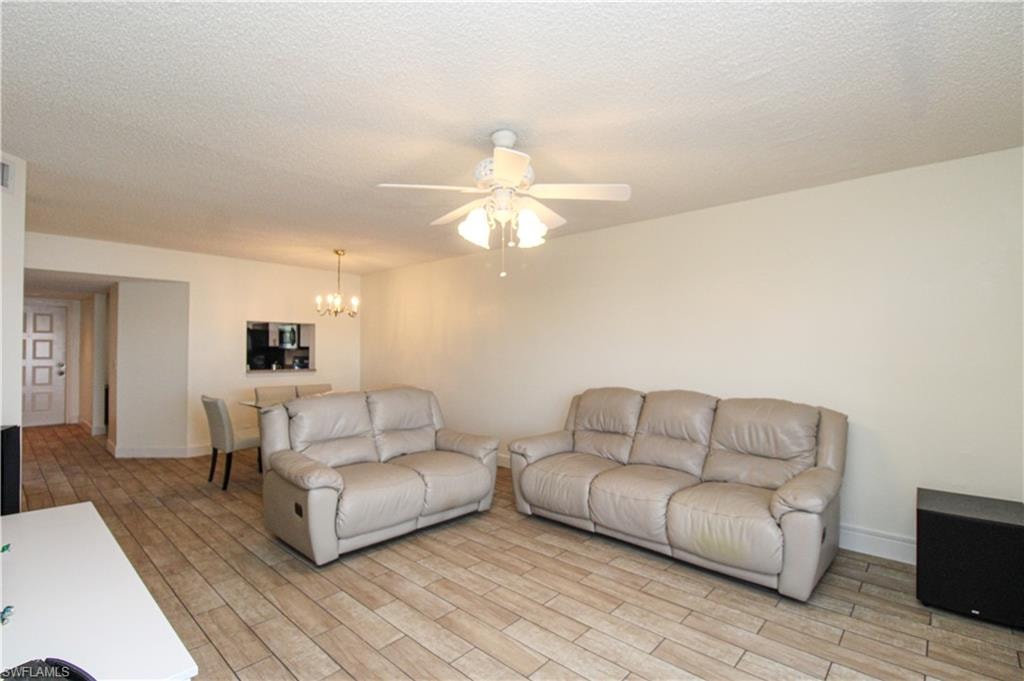 Living room featuring ceiling fan with notable chandelier, light wood-type flooring, and a textured ceiling