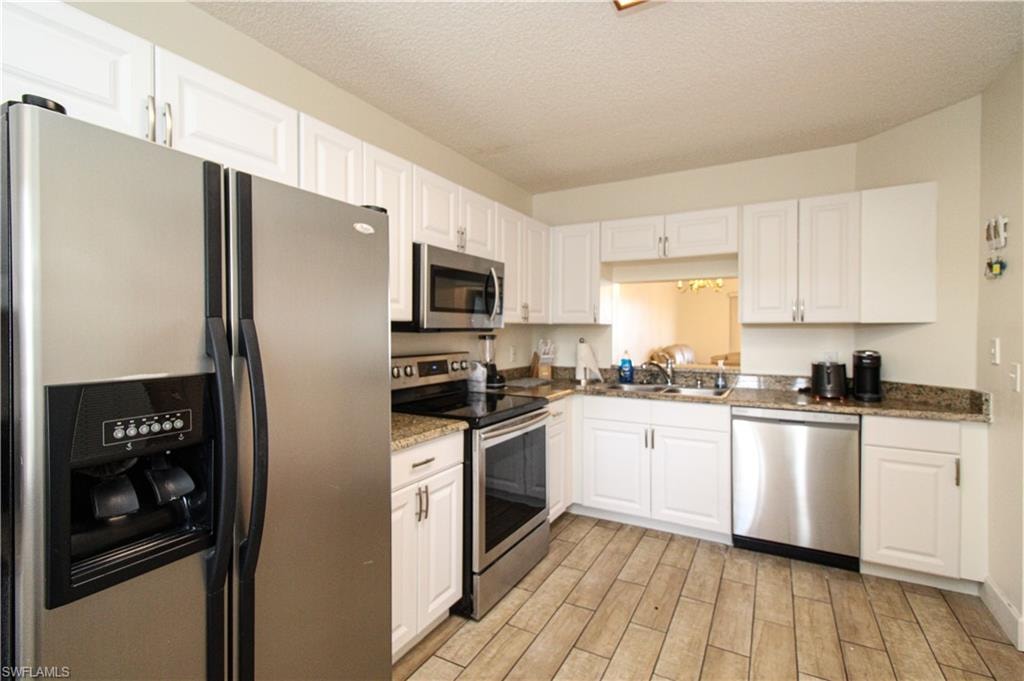 Kitchen with light wood-type flooring, a textured ceiling, sink, white cabinets, and stainless steel appliances