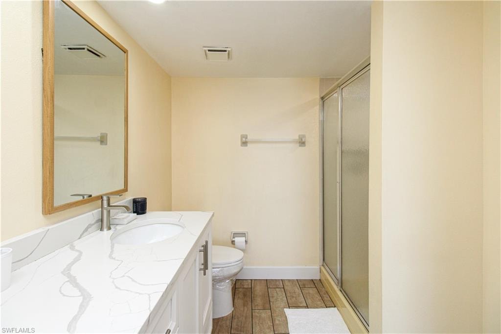Bathroom featuring wood-type flooring, an enclosed shower, vanity, and toilet