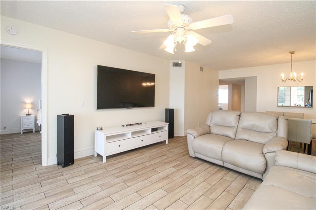 Living room with ceiling fan with notable chandelier, a textured ceiling, and light hardwood / wood-style flooring