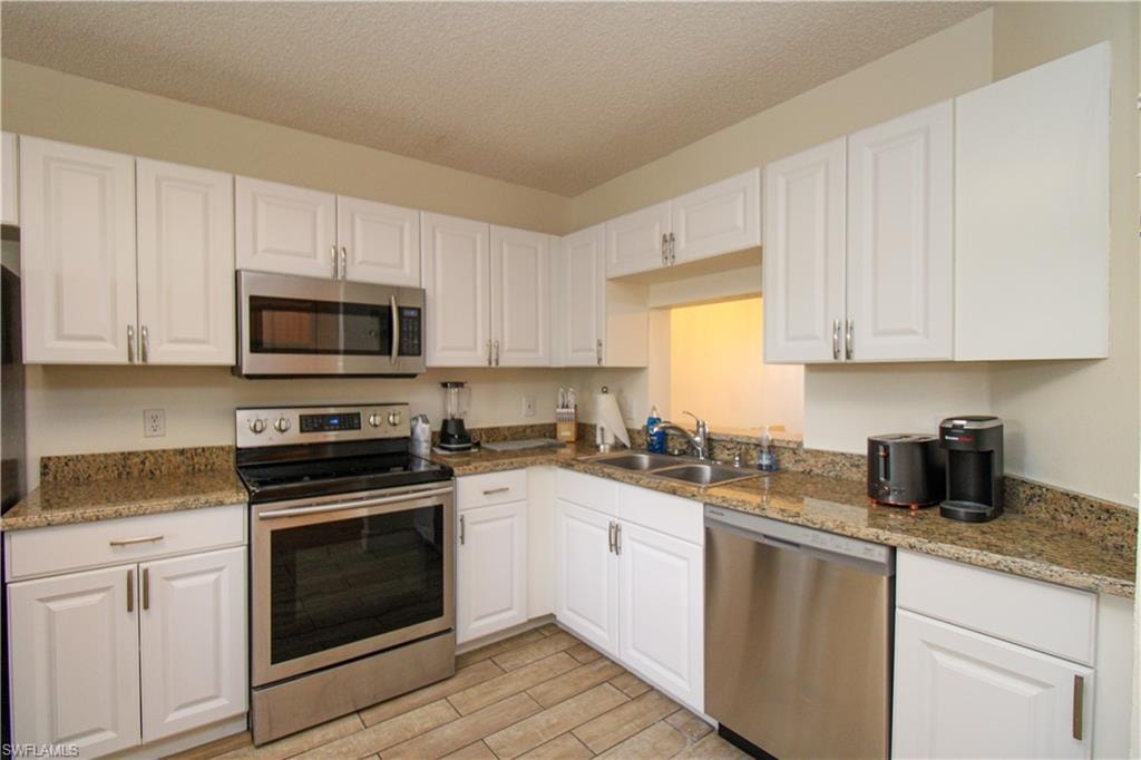 Kitchen with sink, a textured ceiling, light hardwood / wood-style flooring, white cabinetry, and stainless steel appliances