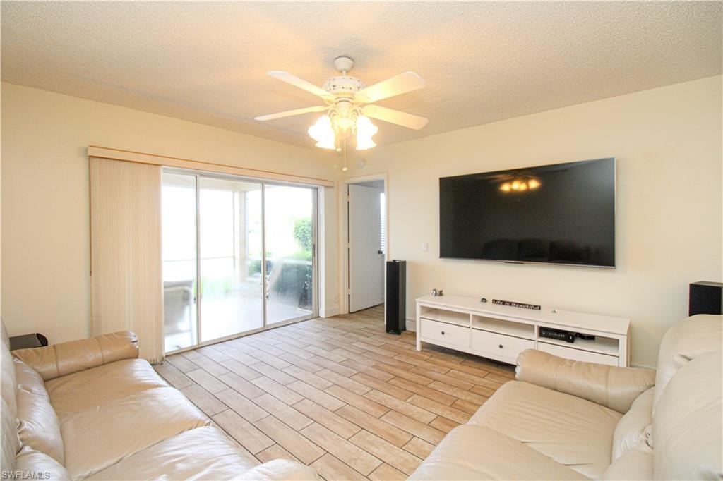 Living room with ceiling fan, a textured ceiling, and light hardwood / wood-style flooring