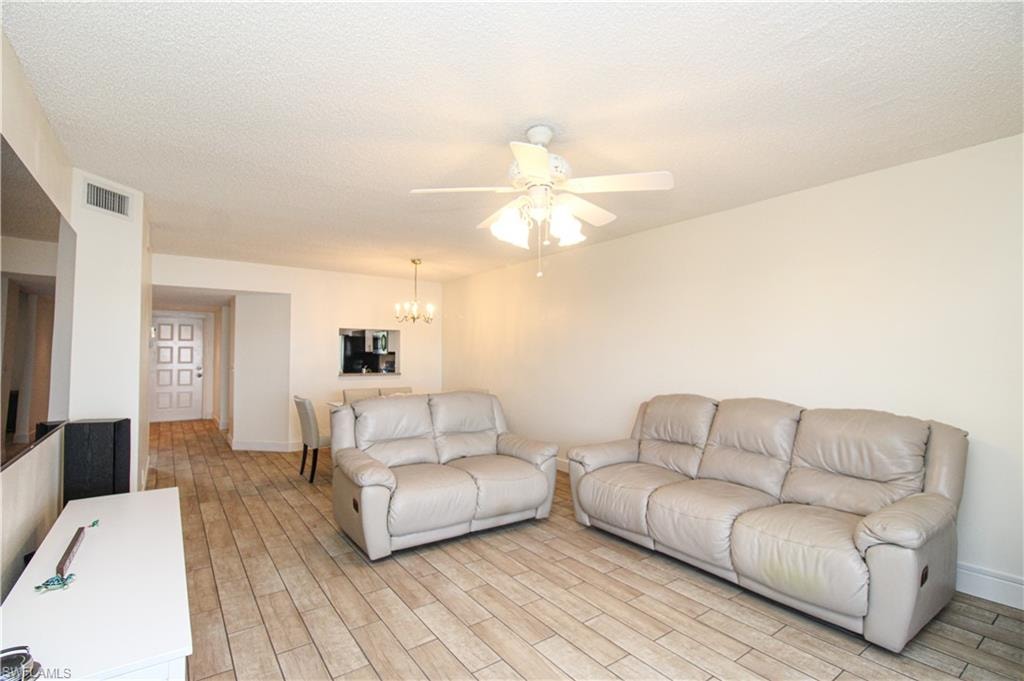 Living room featuring ceiling fan with notable chandelier, light hardwood / wood-style floors, and a textured ceiling