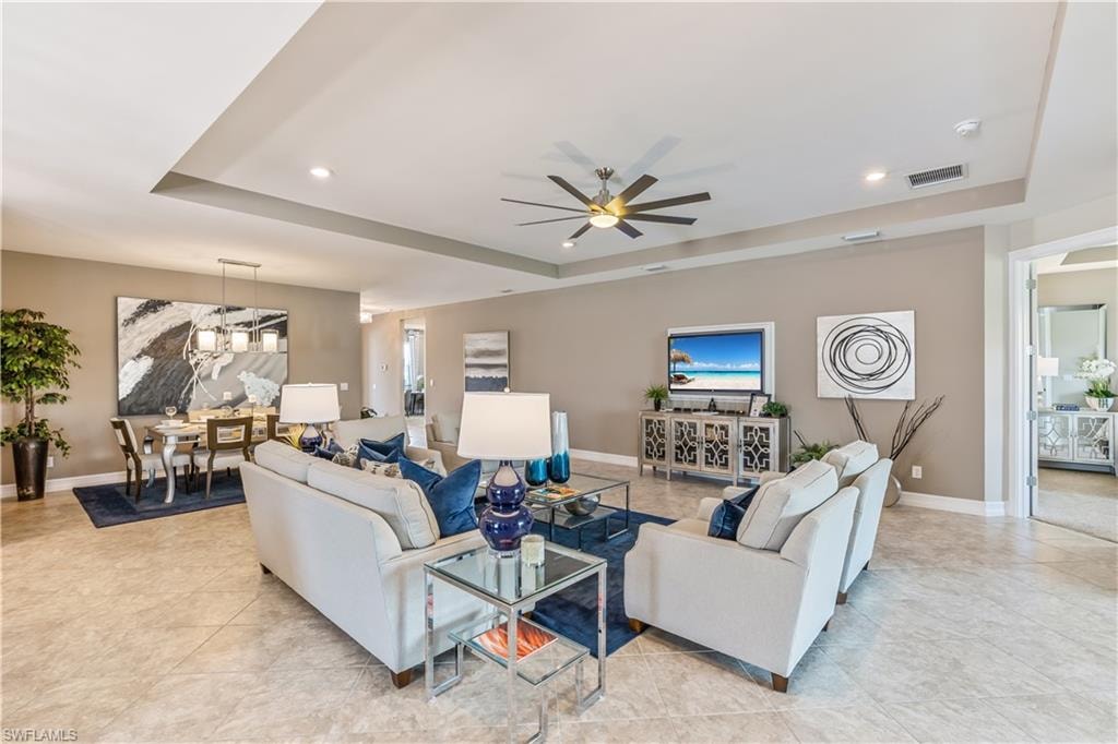 Sophisticated open-concept living space featuring dual cream upholstered seating arrangements anchored by a glass-top cocktail table, recessed ceiling lighting, and a coffered ceiling with integrated ceiling fan