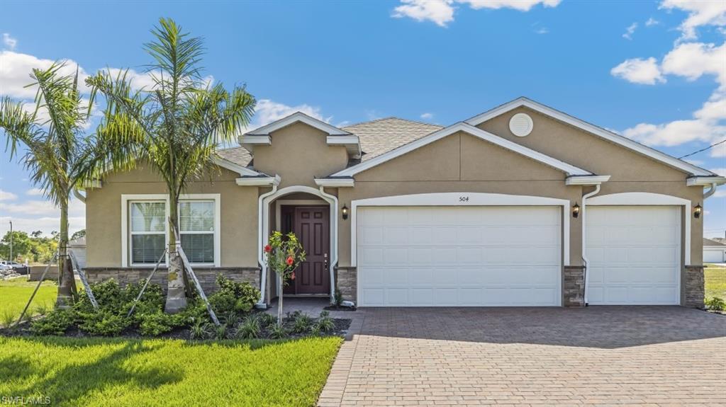 Model Home - Stucco exterior featuring stone veneer accents, a covered entry with a paneled front door, and a paver driveway leading to two garage doors