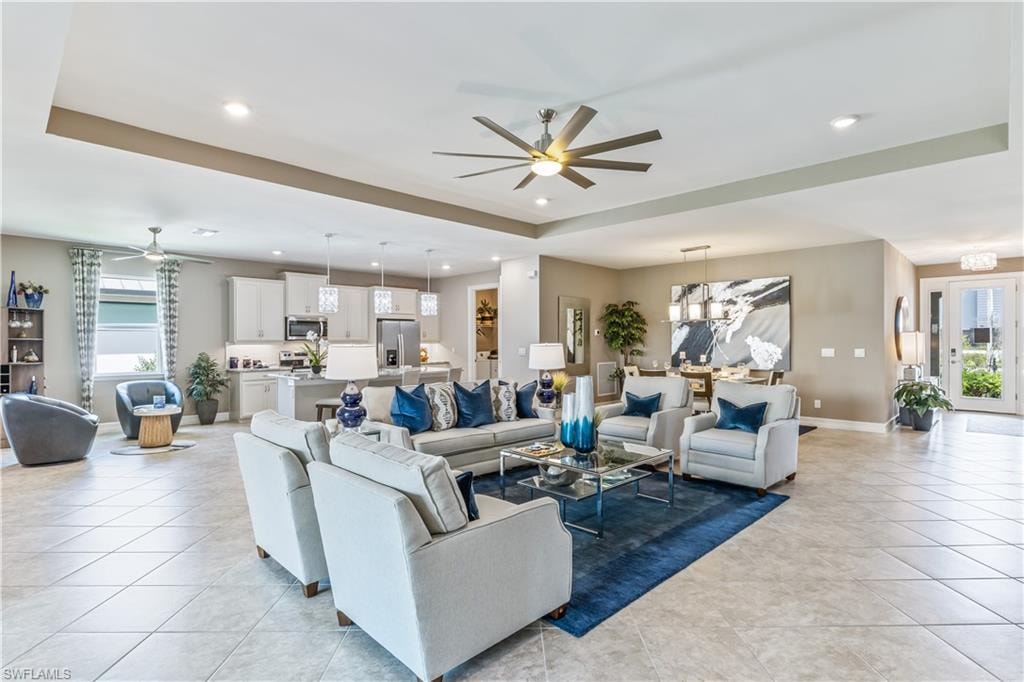 Open-concept living area showcasing soaring ceilings with architectural tray detail, recessed lighting, and a ceiling fan with integrated light fixture